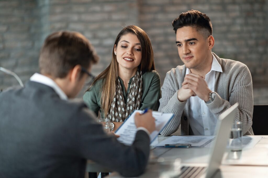 Happy couple and their bank manager going through paperwork on a meeting.